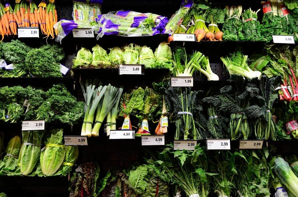 Supermarket produce shelves stocked with kale, leeks, lettuce, carrots and other fresh leafy vegetables
