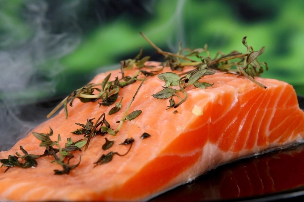 Salmon fillet topped with fresh thyme sprigs, with wisps of steam rising against a blurred green background.