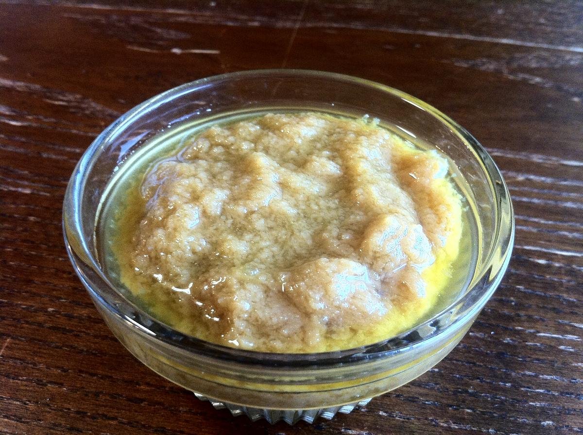 Minced garlic in a glass dish of olive oil on a dark wooden table