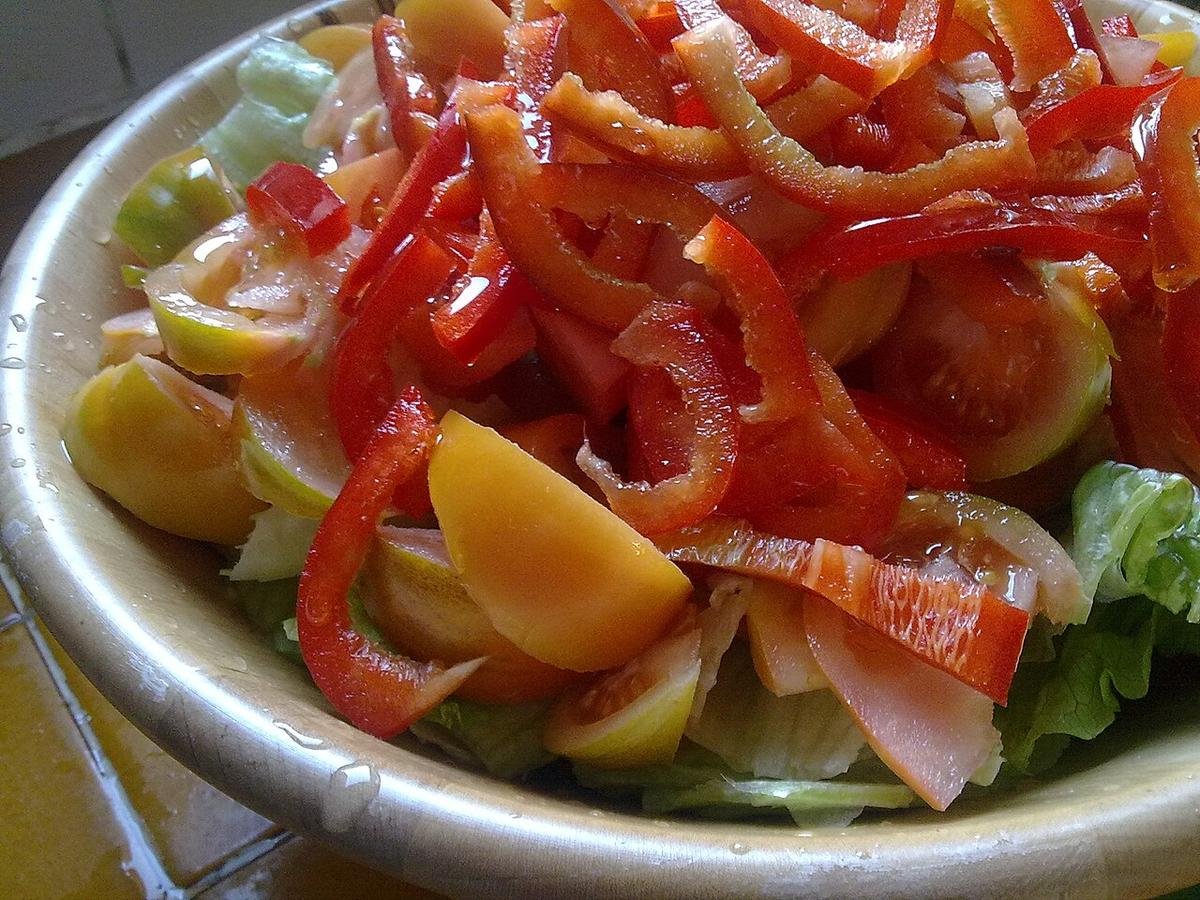 Bowl of salad with red pepper strips, yellow tomato pieces and lettuce, lightly coated in dressing.