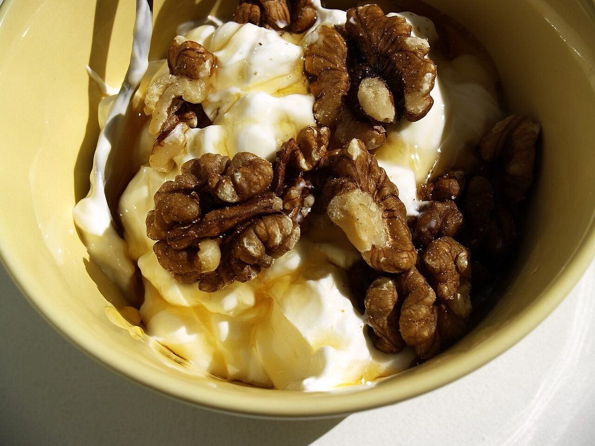 A yellow bowl of white yogurt topped with walnut pieces and a drizzle of golden honey.