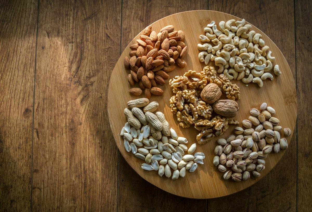 Round wooden board holding almonds, cashews, walnuts, peanuts and pistachios on a rustic wooden table