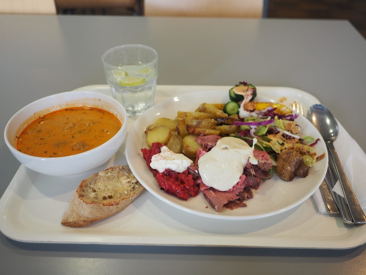 Glass of water with lemon slices beside a bowl of tomato soup and a plate of roast beef, potatoes and salad