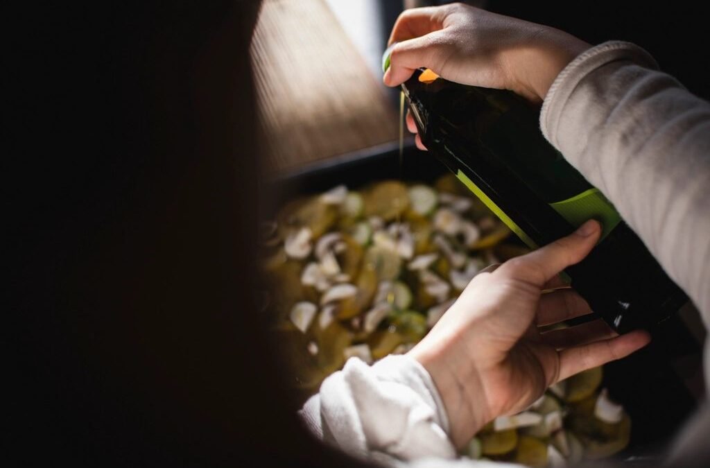 Hands pour olive oil over sliced mushrooms and vegetables in a pan, illustrating a mediteranian diet for menoapuse