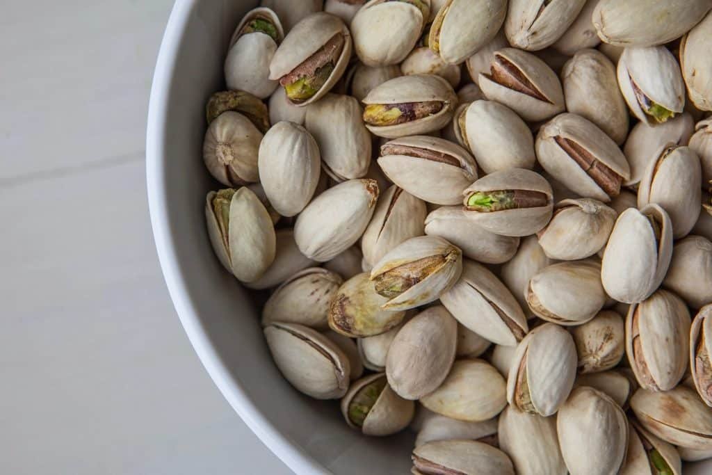 Pistachios in their shells in a white bowl, with several split open to show green kernels