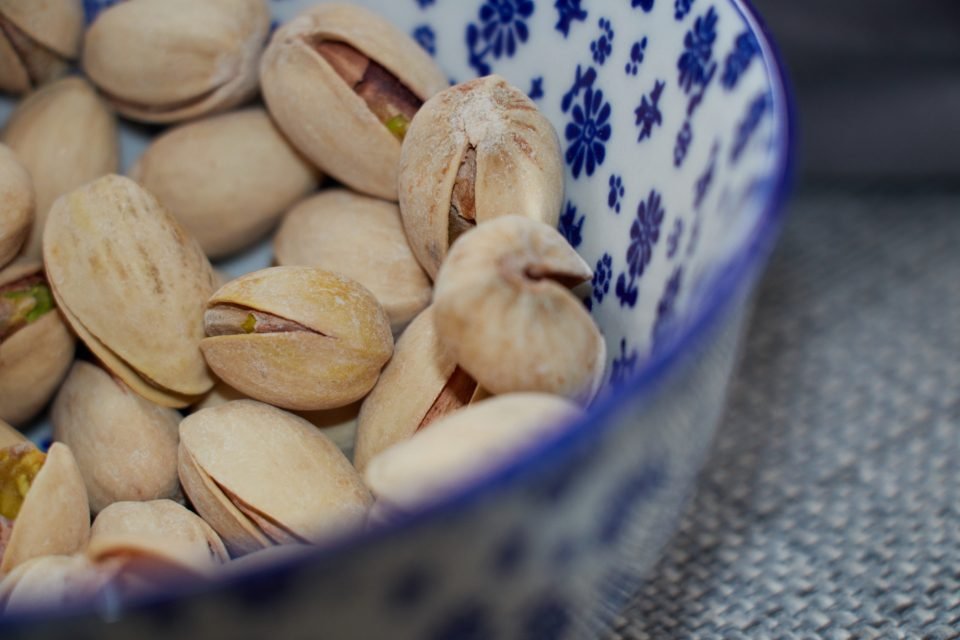 Blue-and-white patterned bowl of partly open pistachios in shells, illustrating pistachio benefits as a snack.
